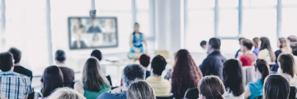 Q-SYS audio in a large room: a presenter addressing an audience, with remote attendees on screen