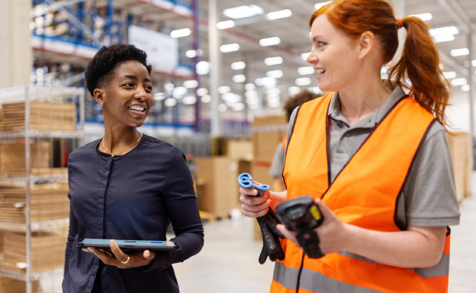 Two warehouse workers talking, one holding a rugged tablet and the other a handheld scanner